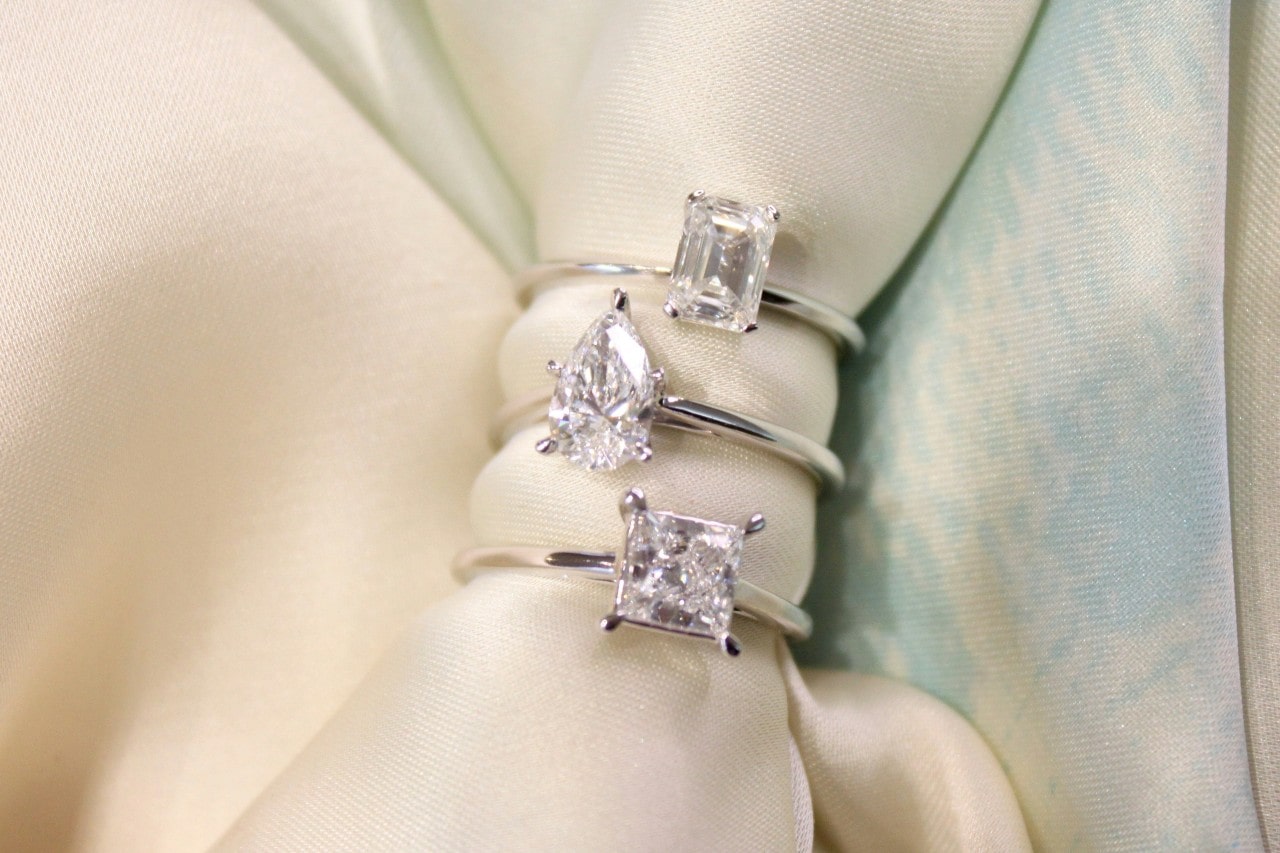 Simple engagement rings with different cut stones stacked on a piece of fabric. Simple engagement rings with different cut stones stacked on a piece of fabric.