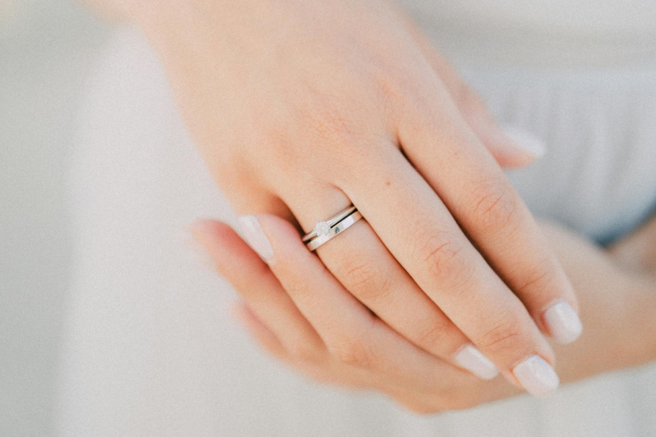A close-up of a bride’s hands, one adorned with a simple engagement ring and wedding band. A close-up of a bride’s hands, one adorned with a simple engagement ring and wedding band.