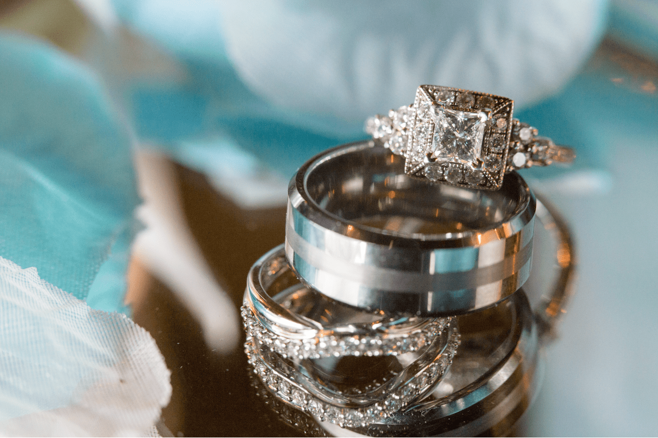 a vintage engagement ring sits on a pile of wedding bands among flowers. a vintage engagement ring sits on a pile of wedding bands among flowers.